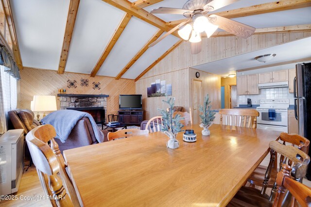 dining area with a stone fireplace, vaulted ceiling with beams, ceiling fan, and light hardwood / wood-style floors