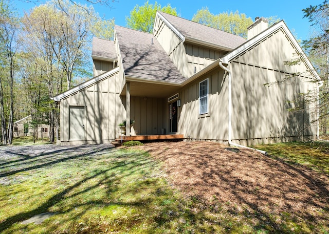 355 Windy Bush Rd, Pocono Pines, PA 18350 - view of home's exterior with a chimney, a shingled roof, an attached garage, board and batten siding, and a lawn