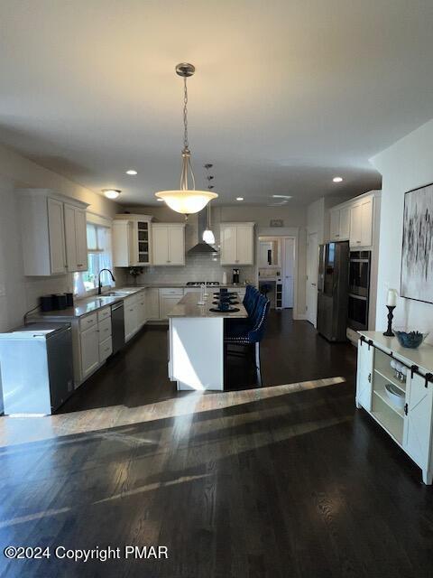 kitchen featuring black appliances, white cabinets, a kitchen island, decorative light fixtures, and wall chimney exhaust hood