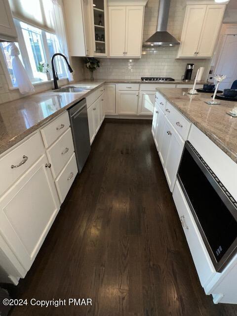 kitchen with dark hardwood / wood-style floors, decorative light fixtures, white cabinets, light stone counters, and a center island with sink