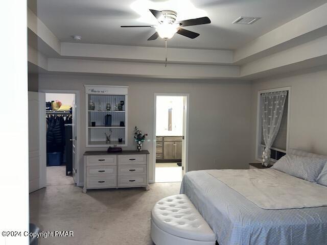 carpeted bedroom with ensuite bath, a spacious closet, a raised ceiling, a closet, and ceiling fan