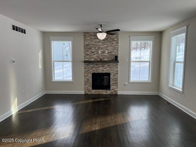 unfurnished living room featuring a stone fireplace, dark wood-type flooring, and ceiling fan