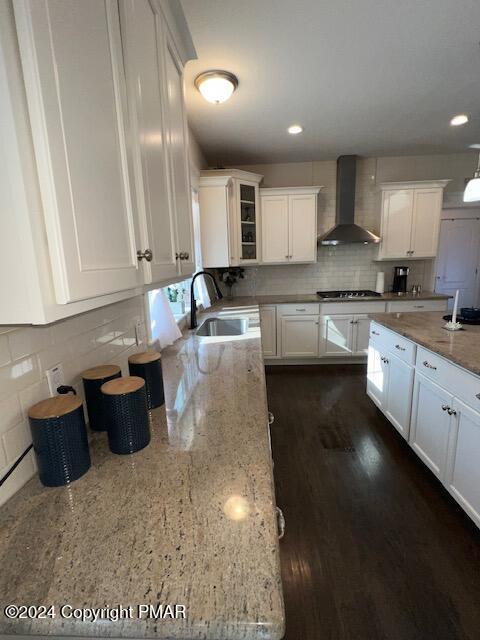 kitchen with white cabinetry, stainless steel gas cooktop, decorative backsplash, and wall chimney exhaust hood