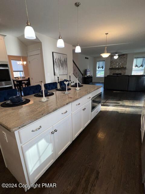 kitchen featuring pendant lighting, white cabinetry, light stone counters, dark wood-type flooring, and a center island with sink