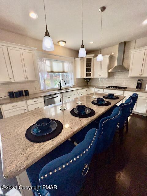 kitchen featuring appliances with stainless steel finishes, white cabinetry, sink, a center island, and wall chimney exhaust hood