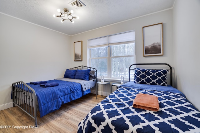 bedroom with ornamental molding, light wood-style flooring, a textured ceiling, and visible vents