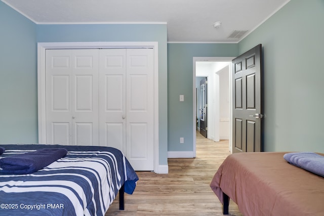 bedroom featuring crown molding, a closet, visible vents, light wood-style flooring, and baseboards