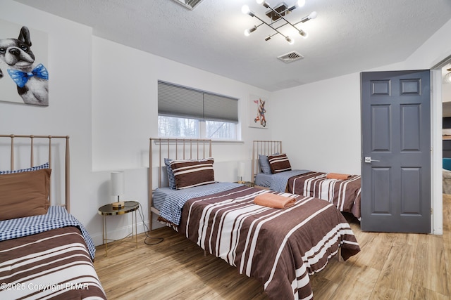 bedroom featuring visible vents, a textured ceiling, baseboards, and wood finished floors