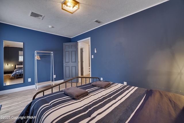 bedroom with visible vents, a textured ceiling, baseboards, and wood finished floors