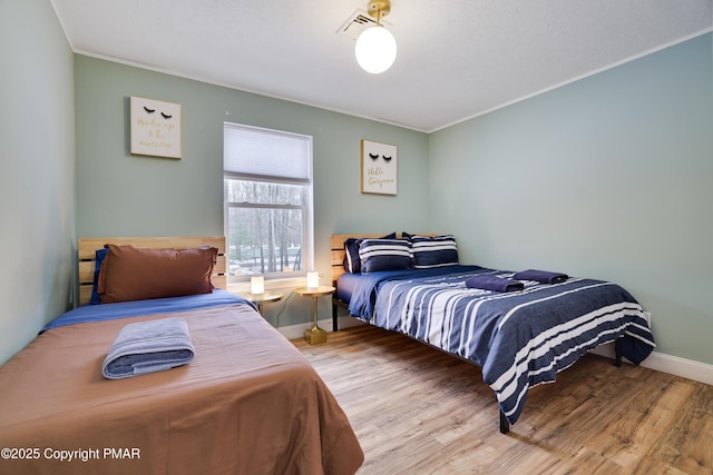 bedroom featuring baseboards, wood finished floors, visible vents, and crown molding