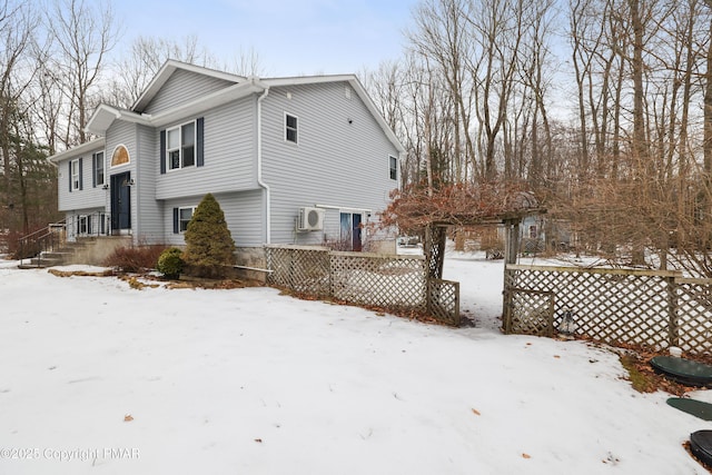 view of snow covered exterior featuring a wall unit AC and fence