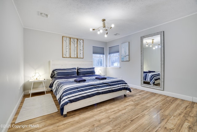 bedroom featuring visible vents, an inviting chandelier, a textured ceiling, wood finished floors, and baseboards