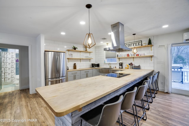 kitchen featuring island exhaust hood, light wood finished floors, open shelves, tasteful backsplash, and freestanding refrigerator