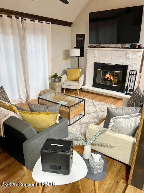 living area with light wood finished floors, a brick fireplace, and vaulted ceiling