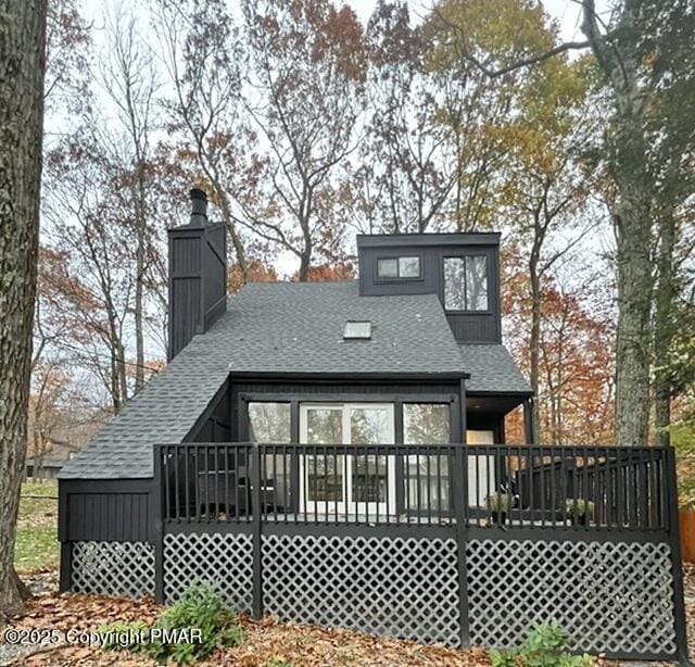 rear view of property featuring a shingled roof, a chimney, and a deck