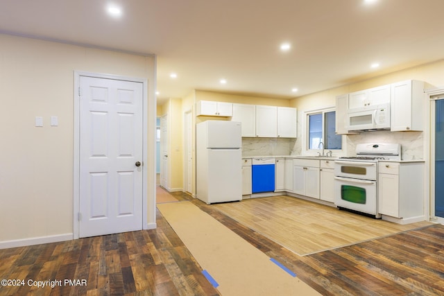 kitchen with a sink, white appliances, backsplash, and wood finished floors