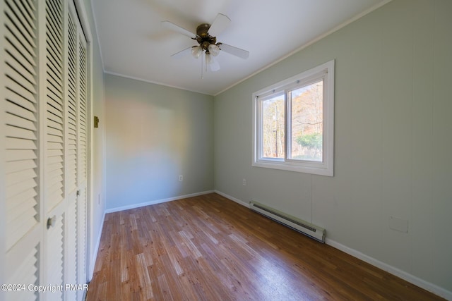 empty room featuring crown molding, a baseboard heating unit, a ceiling fan, wood finished floors, and baseboards