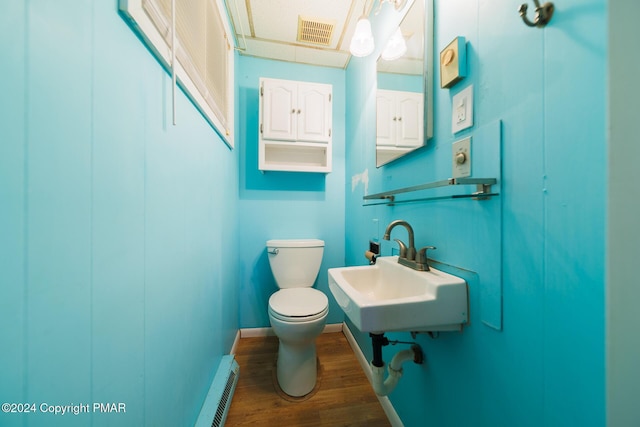 bathroom featuring toilet, a baseboard heating unit, wood finished floors, a sink, and visible vents