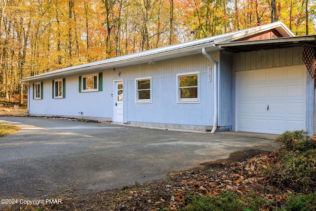 view of front of property featuring a garage, a forest view, aphalt driveway, and metal roof