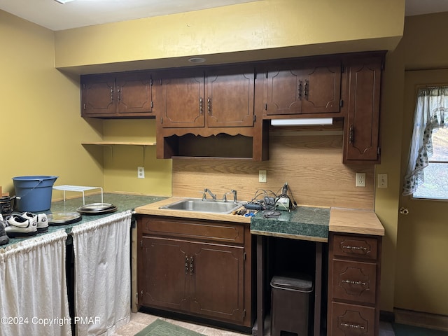 kitchen featuring open shelves, tasteful backsplash, light countertops, a sink, and dark brown cabinets