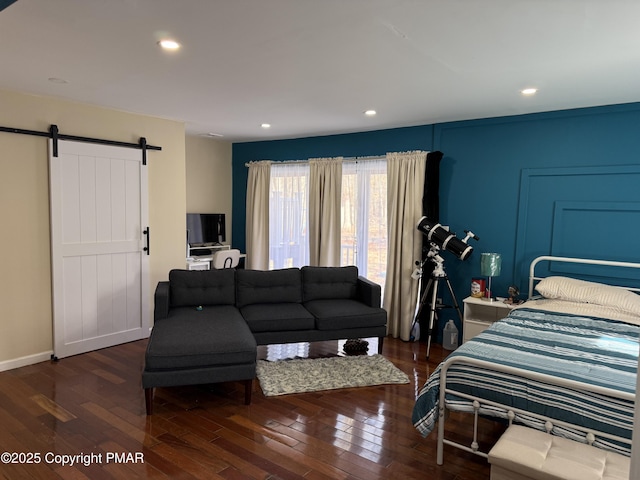 bedroom with a barn door, baseboards, wood-type flooring, and recessed lighting