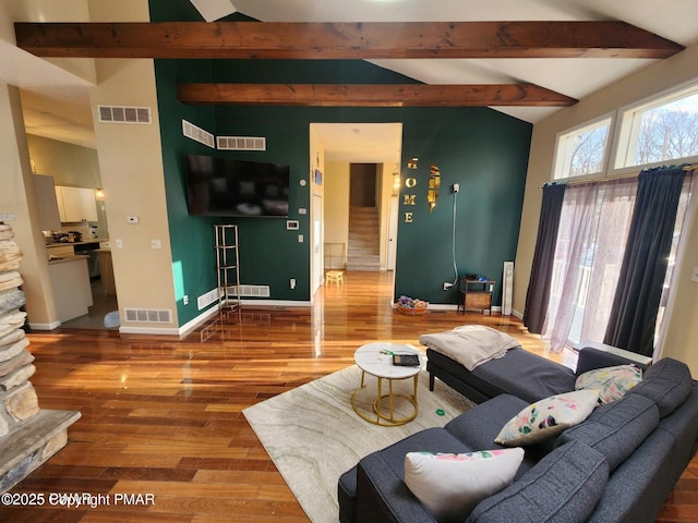 living area featuring lofted ceiling with beams, baseboards, visible vents, and wood finished floors