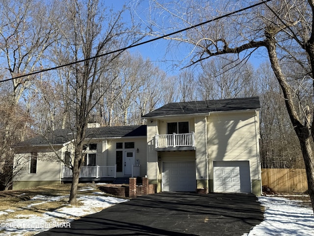 tri-level home featuring aphalt driveway, fence, a balcony, and an attached garage