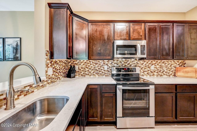 kitchen featuring a sink, dark brown cabinets, appliances with stainless steel finishes, decorative backsplash, and light stone countertops