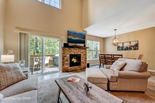 living area with a stone fireplace, a high ceiling, wood finished floors, baseboards, and an inviting chandelier