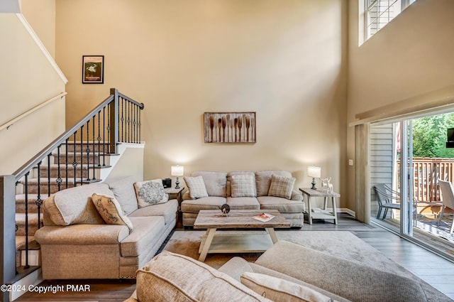 living area with stairway, a healthy amount of sunlight, a towering ceiling, and wood finished floors