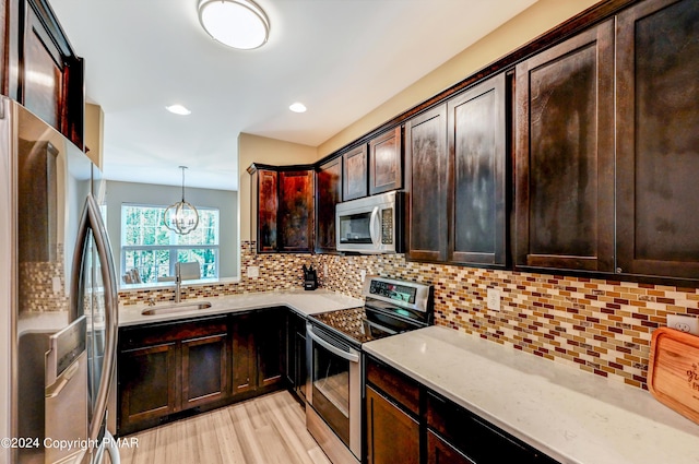 kitchen featuring a sink, light wood-style floors, appliances with stainless steel finishes, backsplash, and light stone countertops