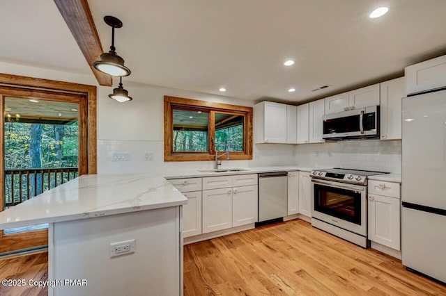 kitchen featuring a peninsula, appliances with stainless steel finishes, a sink, and a wealth of natural light