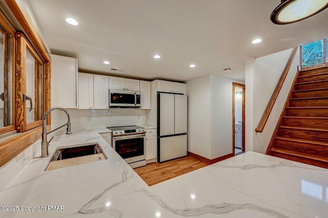 kitchen featuring a sink, light stone countertops, stainless steel appliances, white cabinetry, and backsplash