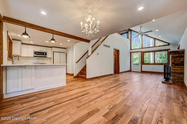 unfurnished living room with beam ceiling, stairway, high vaulted ceiling, light wood-type flooring, and ceiling fan with notable chandelier