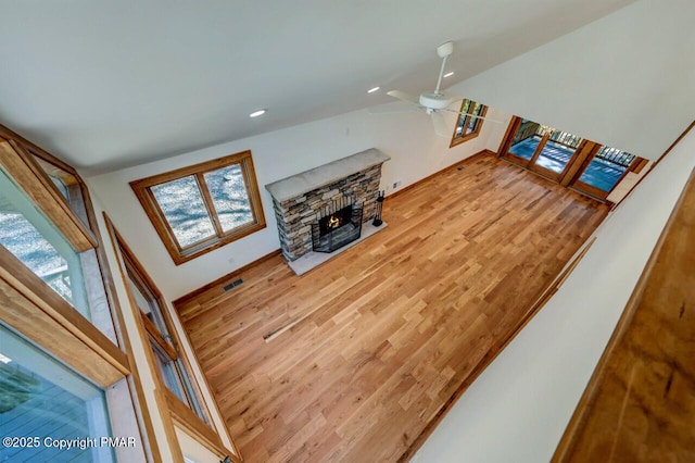 living area featuring visible vents, lofted ceiling, ceiling fan, wood finished floors, and a stone fireplace