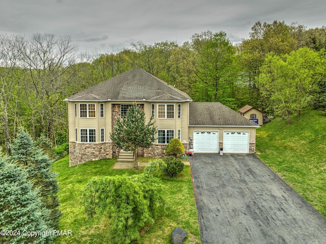 view of front of property featuring an attached garage, a front yard, stone siding, driveway, and a forest view