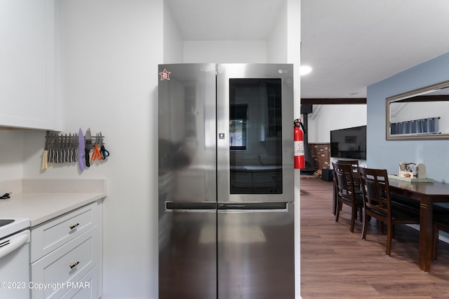 kitchen featuring electric stove, wood finished floors, light countertops, refrigerator with glass door, and white cabinetry