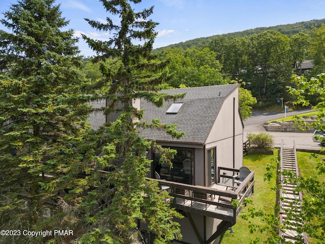 rear view of property with a forest view, a wooden deck, and roof with shingles