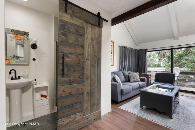 living area featuring lofted ceiling with beams, a barn door, a textured ceiling, and wood finished floors