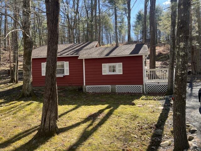 view of home's exterior featuring a wooden deck, a lawn, and roof with shingles