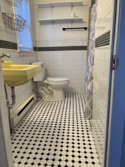 full bath featuring a baseboard heating unit, toilet, a shower with shower curtain, tile patterned floors, and tile walls