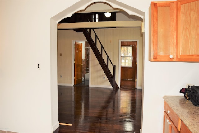 hallway featuring arched walkways, stairs, baseboards, and dark wood-style flooring