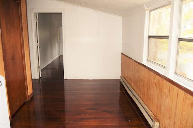 hallway featuring a wainscoted wall, a baseboard heating unit, wooden walls, crown molding, and dark wood-style flooring