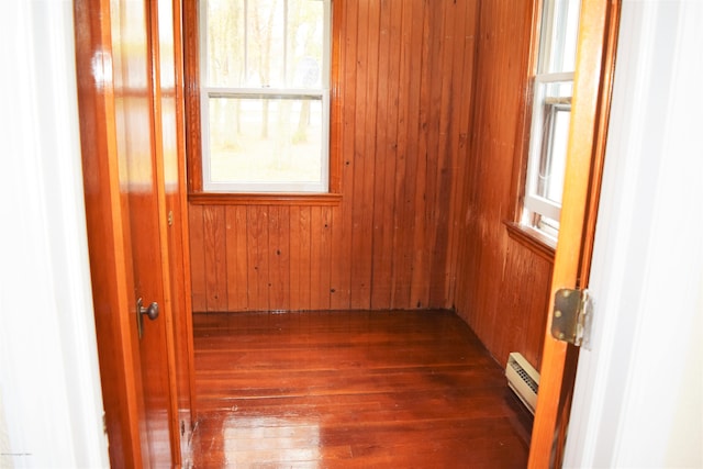 empty room with wood walls, a baseboard radiator, and wood-type flooring