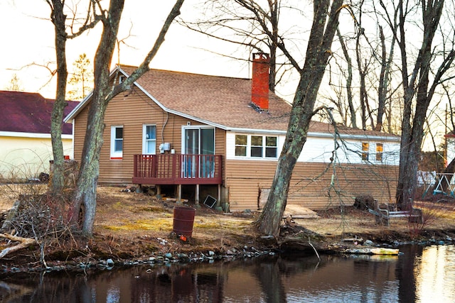 back of property featuring a deck with water view, roof with shingles, and a chimney