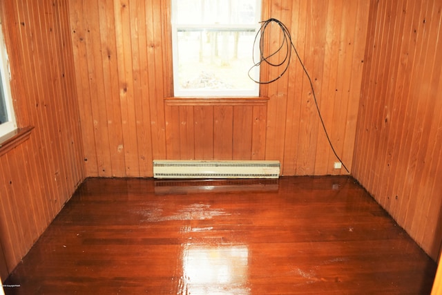 empty room with baseboard heating, wooden walls, and hardwood / wood-style flooring