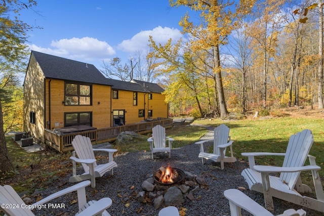 back of house with a fire pit, a deck, a lawn, and a shingled roof