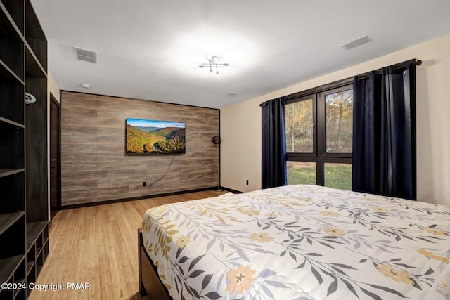 bedroom featuring wood walls, an accent wall, visible vents, and wood finished floors