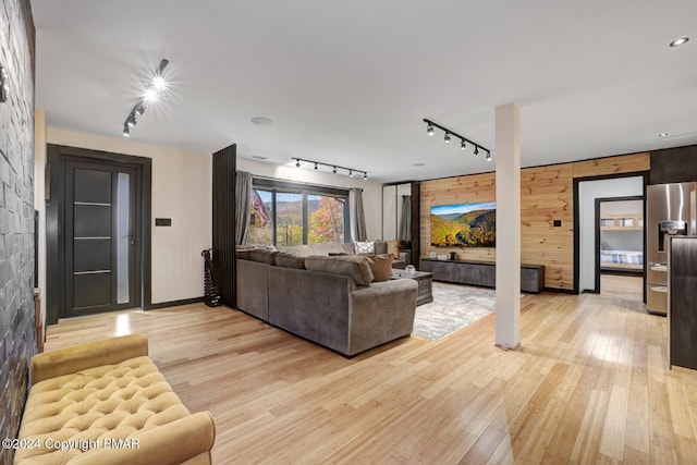 living room featuring light wood-style flooring, wooden walls, and track lighting