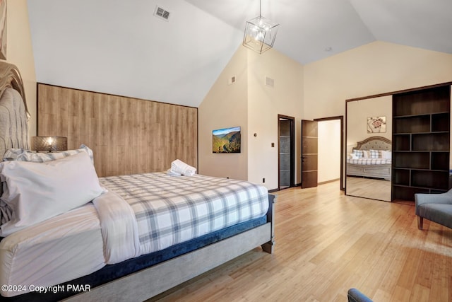 bedroom featuring high vaulted ceiling, wood finished floors, visible vents, and a notable chandelier